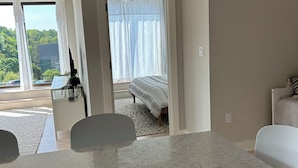 A modern kitchen with a marble countertop, white chairs, and a view of a bedroom with a bed and curtains. - Sunny downtown Belfast apartment with water view, right on Main St near eateries (Belfast)