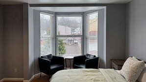 A bedroom with a large bay window, a bed with a green bedspread, two black chairs, and a small table. - Stylish 2-bedroom apartment with WiFi, AC in fabulous downtown French Lick (French Lick)