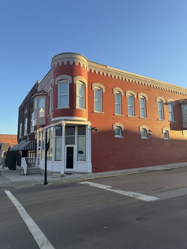 A red brick building with a corner entrance, multiple windows, and a small porch area.