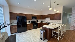 A modern kitchen with wooden cabinets, a black refrigerator, a microwave, a stove, and a sink. There are pendant lights, a trash can, and a small island with bar stools. - Stylish 2-bedroom apartment with WiFi, AC in fabulous downtown French Lick (French Lick)