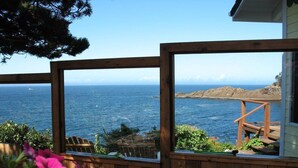 A wooden deck with a view of the ocean, a wooden structure, and pink flowers in the foreground. - Ocean Garden Suite at Whales Rendezvous (Depoe Bay)