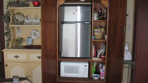 A compact kitchen with a built-in stainless steel refrigerator, a microwave, and a wooden cabinet with shelves holding various kitchen items. - Ocean Garden Suite at Whales Rendezvous (Depoe Bay)