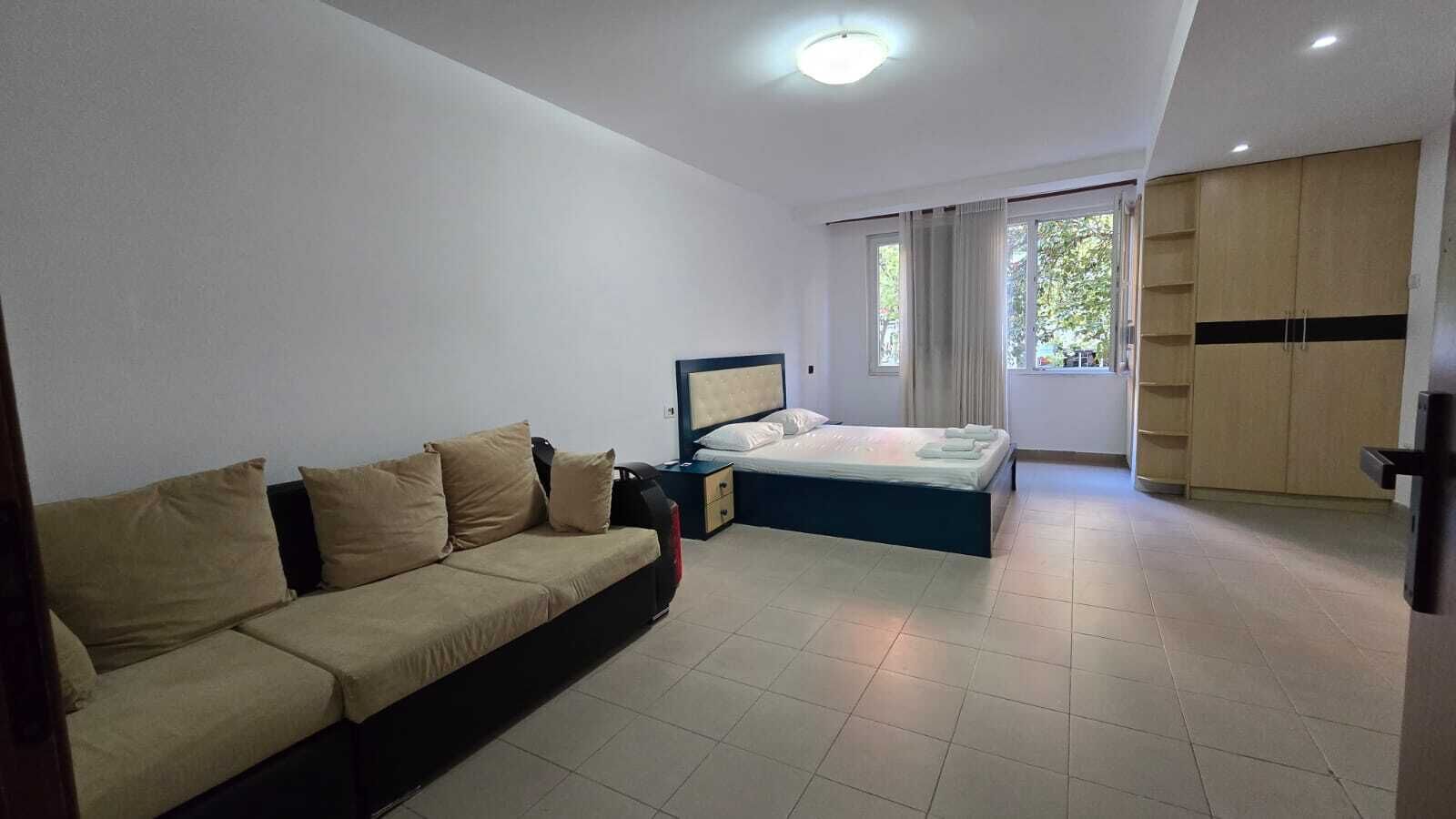 A modern hotel room with a sofa, a bed, a wardrobe, and a window with curtains.