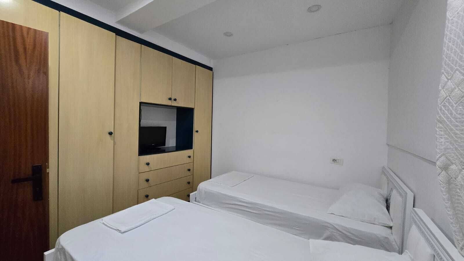 Une petite chambre d’hôtel, composée d’une seule pièce, avec deux lits, une armoire en bois et un petit miroir.