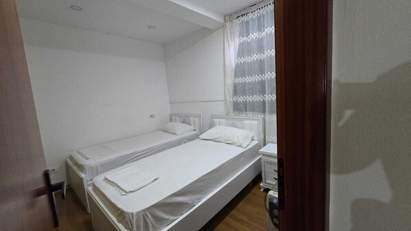 A small, clean room with two single beds, a bedside table, and a window with curtains. - Tirent Apartment-Cozy 2-Bedroom Stay in Don Bosko (Tirana)