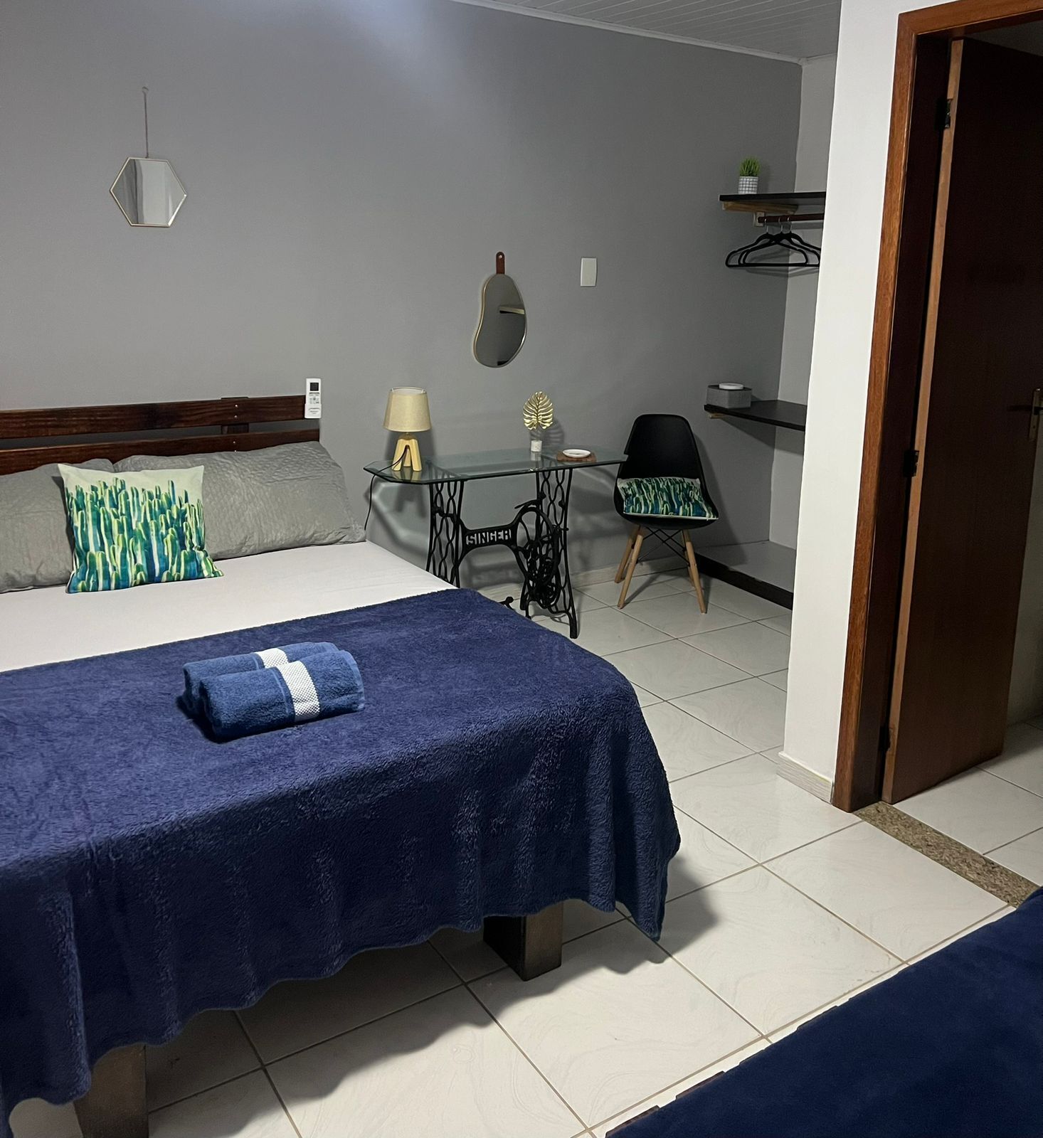 A bedroom with a bed, a small table with a lamp, a chair, and a mirror on the wall.
