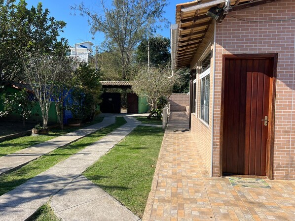 A residential property with a paved driveway leading to a brick entrance, a covered patio area, and a small garden with various plants. - Pousada Arara Búzios (Buzios)