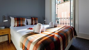 A hotel room with a bed, pillows, a blanket, a nightstand, a lamp, and a view of the outside.