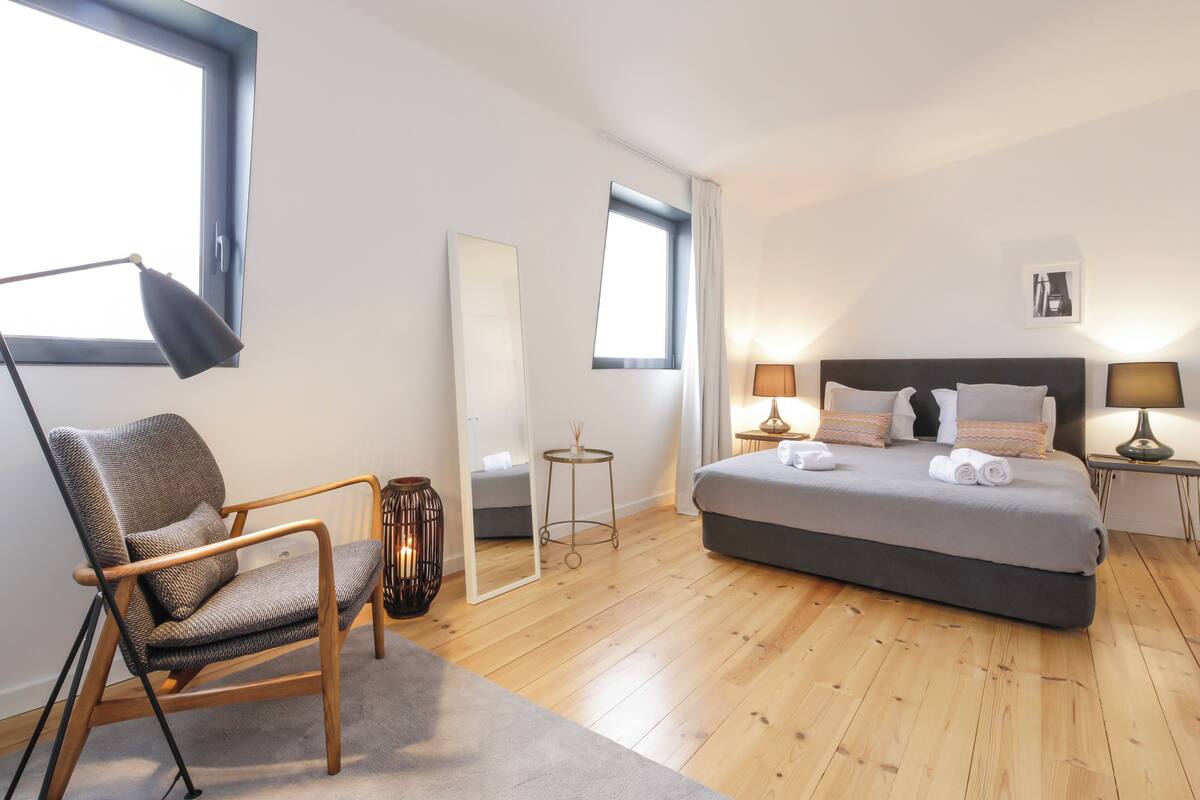 Une chambre moderne avec un grand lit, une chaise, une lampe de bureau et un miroir.