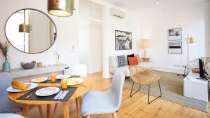 A modern living room with a dining area, featuring a round table, chairs, a sofa, and a large mirror.
