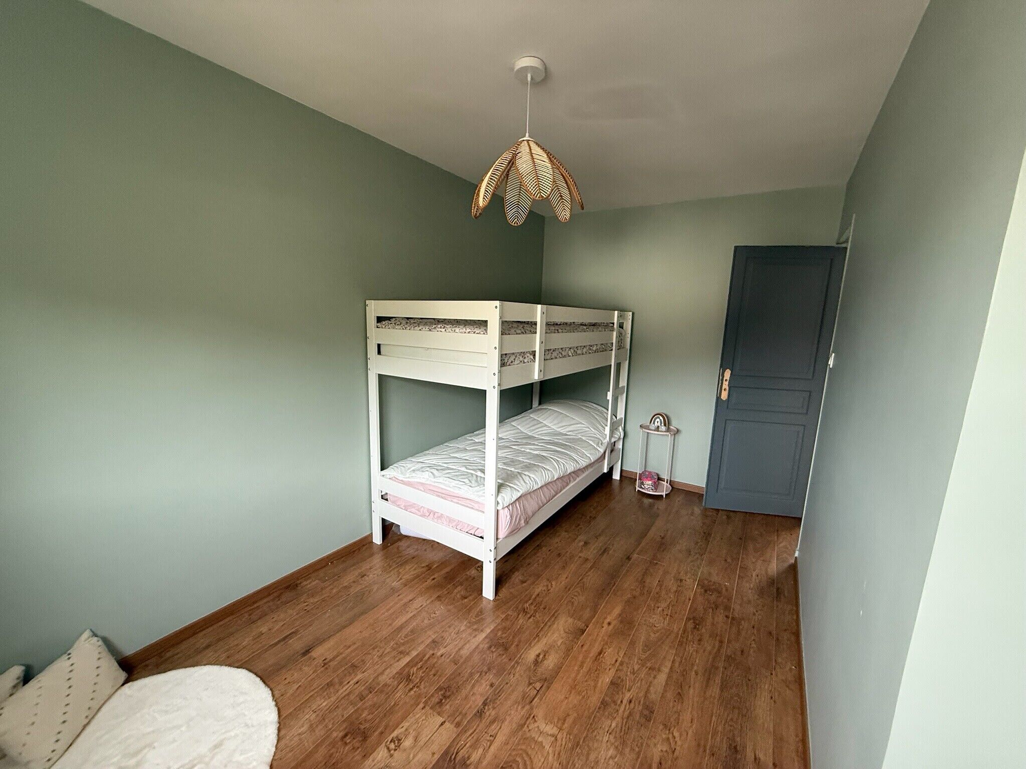 A room with a bunk bed, a small table, a hanging light fixture, and a door.