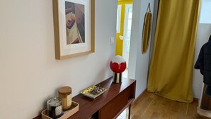 Ein Zimmer mit einem Holzkonsolentisch, einem gerahmten Bild, einem gelben Vorhang und einer Tür zu einem anderen Raum.