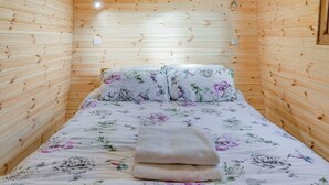 Una habitación pequeña y acogedora con paredes de madera y una cama con ropa de cama estampada con flores.