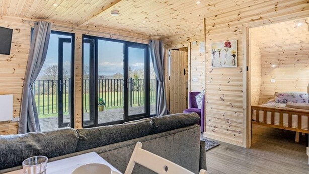 Una cabaña de madera acogedora con comedor, que incluye una mesa dispuesta para dos, una banca y vistas al exterior.