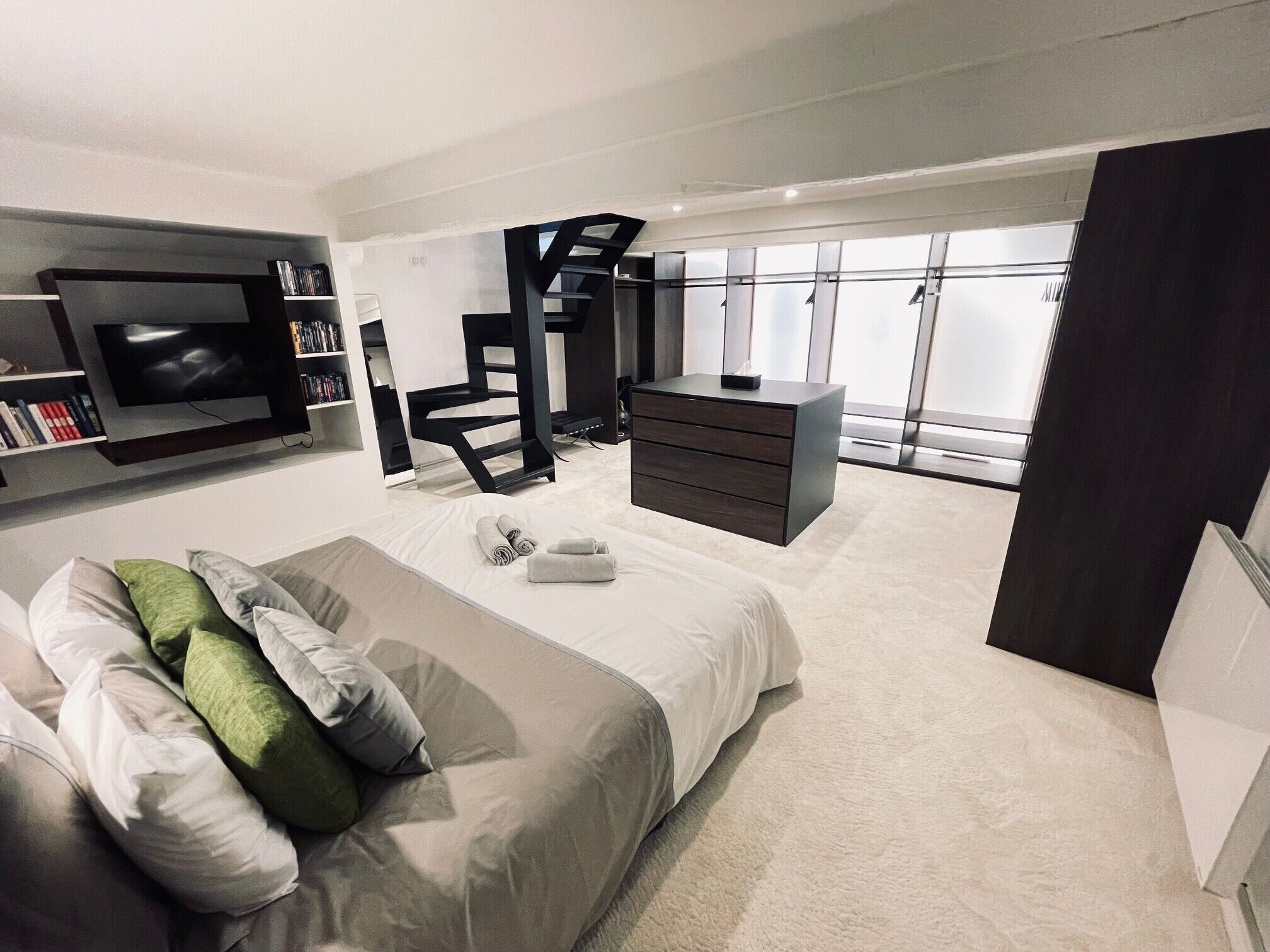 Une chambre à coucher moderne avec un lit, une télévision, un bureau et un escalier.
