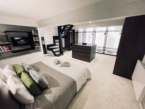 A modern bedroom with a bed, a TV, a desk, and a staircase.