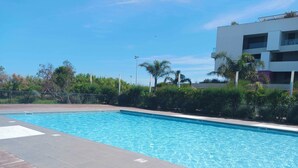 A swimming pool with a tiled deck, surrounded by greenery and a modern building. - Beautiful T2 with pool - near beach (Palavas-les-Flots)
