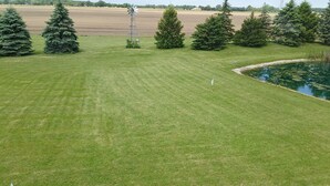 A well-maintained grassy field with a windmill, trees, and a pond.
