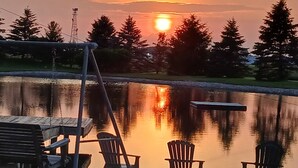A lakeside view with a wooden deck, two Adirondack chairs, and a swing set.