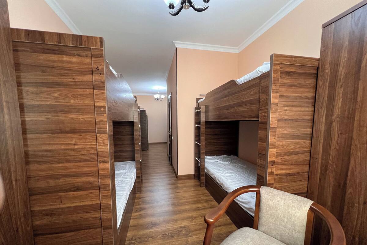 Un dormitorio con literas, piso de madera y una silla.