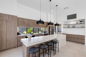 A modern kitchen with a central island, pendant lighting, and a view of greenery outside.