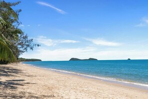 A beach with clear blue water, sandy shore, and palm trees.