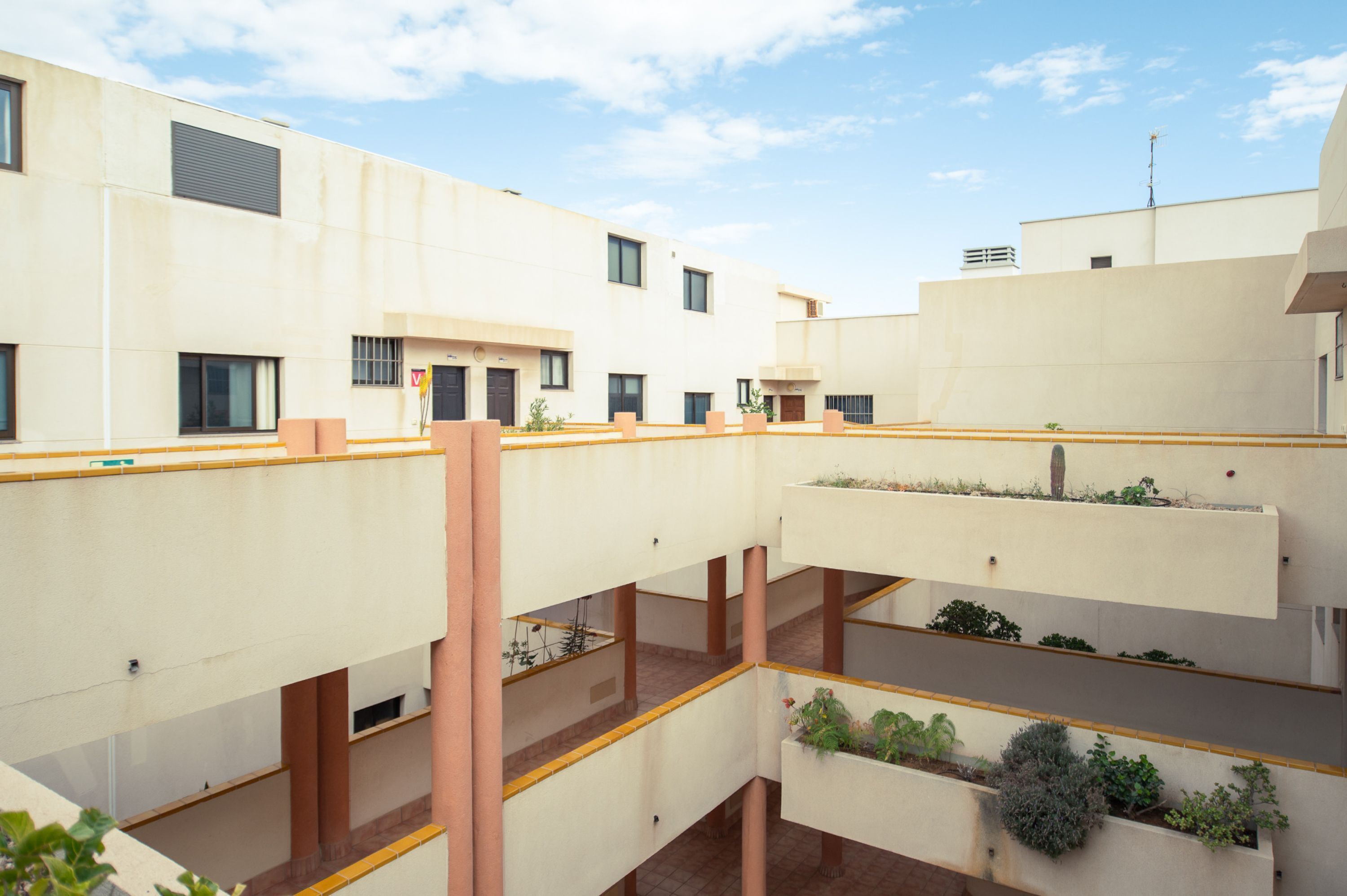 A multi-level building with balconies, each with plants and a yellow railing.