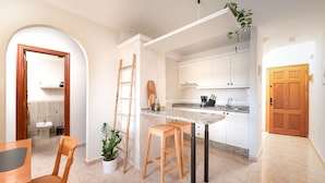A modern kitchen with white cabinets, a granite countertop, and a wooden stool. There is a ladder leaning against the wall and a potted plant on the countertop. - Las Olas Your Retreat in El M Dano (Granadilla de Abona)