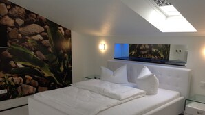 Ein modernes Schlafzimmer mit einem großen Bett, einem Nachttisch, einem an der Wand montierten Fernseher und einem Dachfenster.