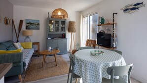 Una sala de estar acogedora con un sofá, una mesa de comedor y un televisor. Se observa una estantería y un cuadro en la pared.