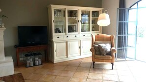 A living room with a television, a cabinet with glass doors, a chair, and a large window. - Maison Roquebeauresse - Piscine privée (Pougnadoresse)
