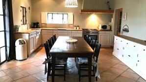 A spacious kitchen with a large dining table, white cabinets, and a hanging light fixture. - Maison Roquebeauresse - Piscine privée (Pougnadoresse)