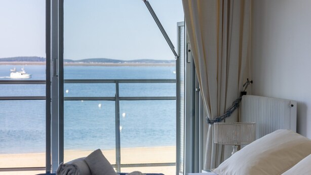 Habitación de hotel con un ventanal que ofrece vistas al mar y un barco.
