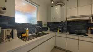 Una cocina moderna con armarios blancos, un lavamanos de acero inoxidable y una campana extractora integrada.