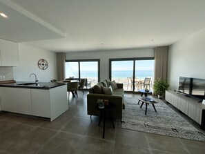 Un espacio de estar moderno con cocina, comedor y asientos junto a un ventanal con vistas al océano.