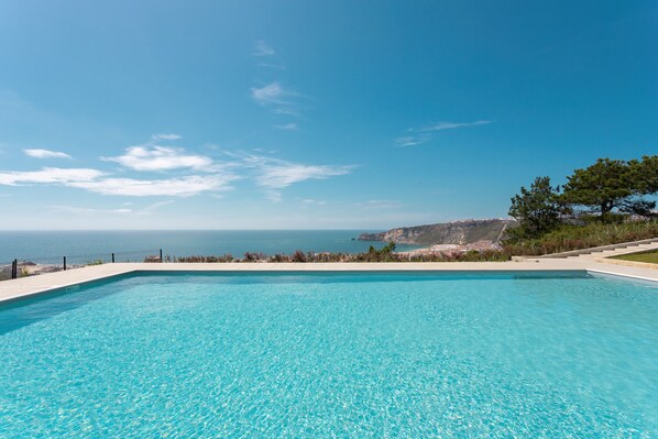 Una piscina azul cristalina con vista al mar y a la costa rocosa.
