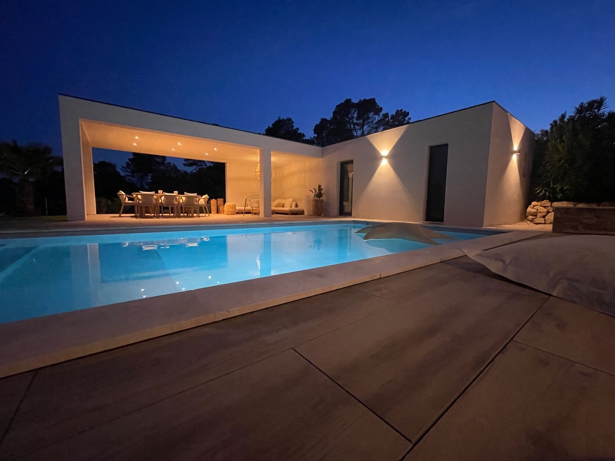 Una casa moderna con piscina, zona de estar exterior y un patio bien iluminado.