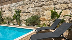 Une piscine entourée de chaises longues, d’un mur de pierre et de différentes plantes.