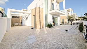 Une maison moderne à deux étages, dotée d’une allée pavée et d’une entrée fermée par un portail.