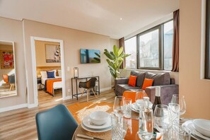 A modern living room with a dining area, a sofa set, and a large window. - CONDE13 Aparthotel Boutique  (Lisboa)