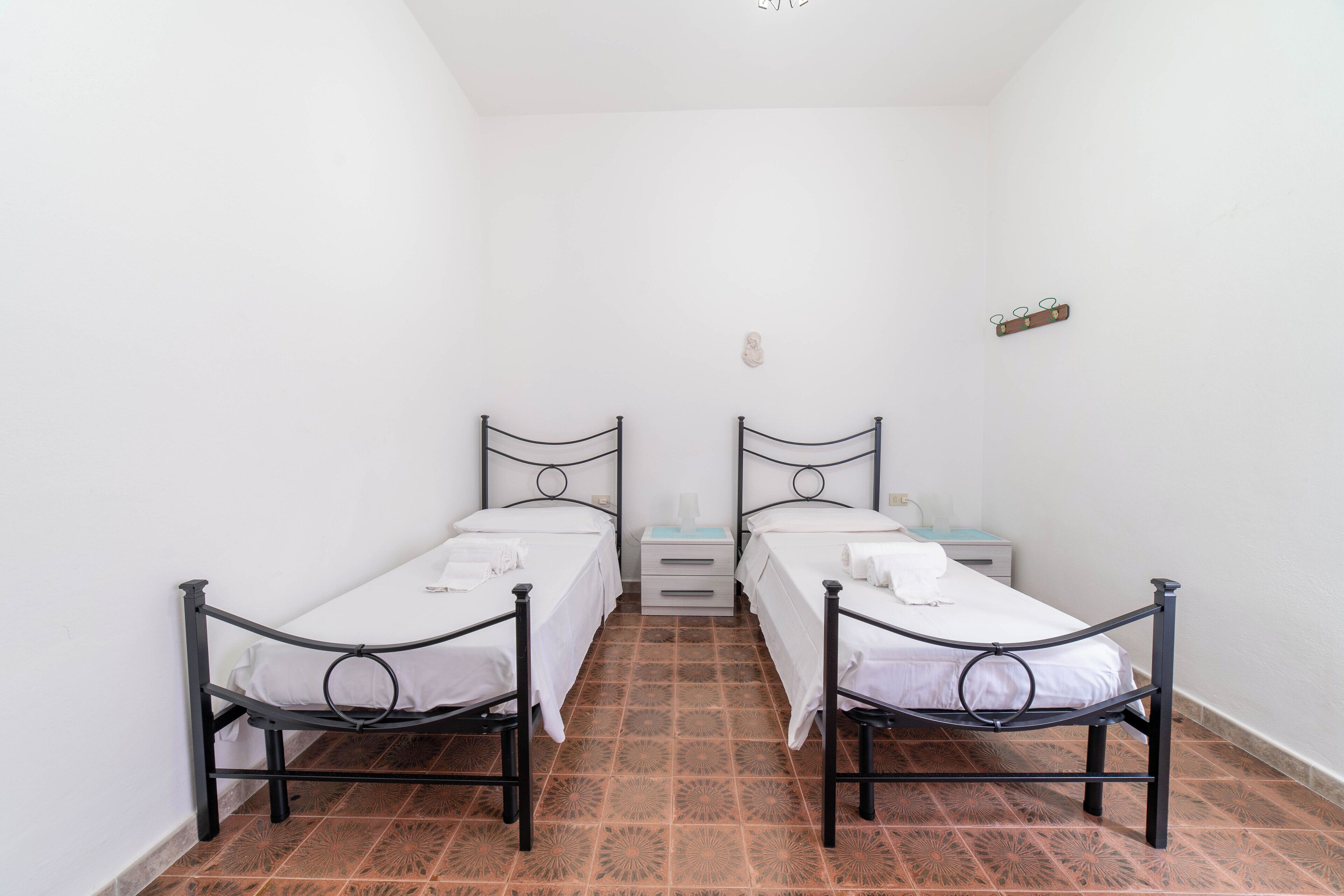 Ein kleines, sauberes Zimmer mit zwei Einzelbetten, einem Nachttisch und einem kleinen Regal.