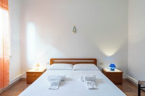 A neatly made bed with white linens and towels, two bedside tables with lamps, and a small decorative item on the wall.