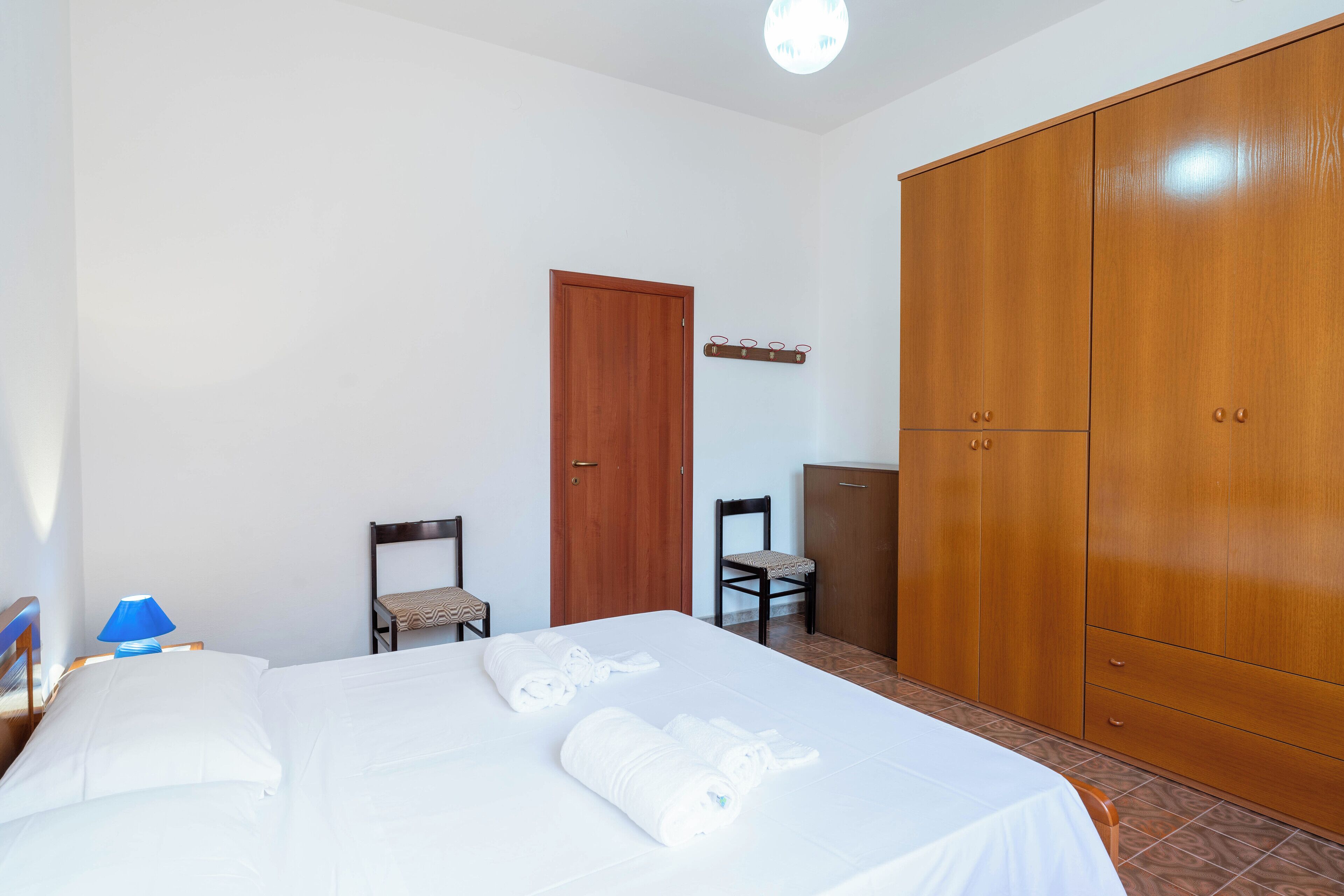Hotellihuone, jossa on sänky, puinen vaatekaappi, tuoli ja työpöytä.
