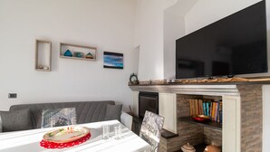 Ein modernes Wohnzimmer mit einem Flachbildfernseher, einem Kamin, einem Esstisch mit roter Tischmatte und einem Bücherregal.