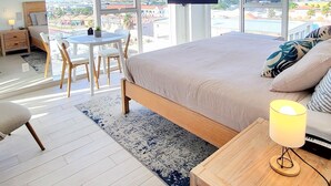 Ein modernes Schlafzimmer mit einem großen Bett, einem an der Wand montierten Fernseher und Blick auf die Stadt durch große Fenster.