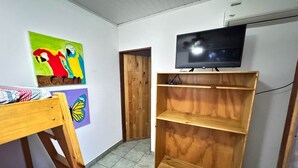 A room with a wooden bed, a TV on a wooden shelf, and colorful wall art. - Delfines del Golfo (Puerto Jimenez)