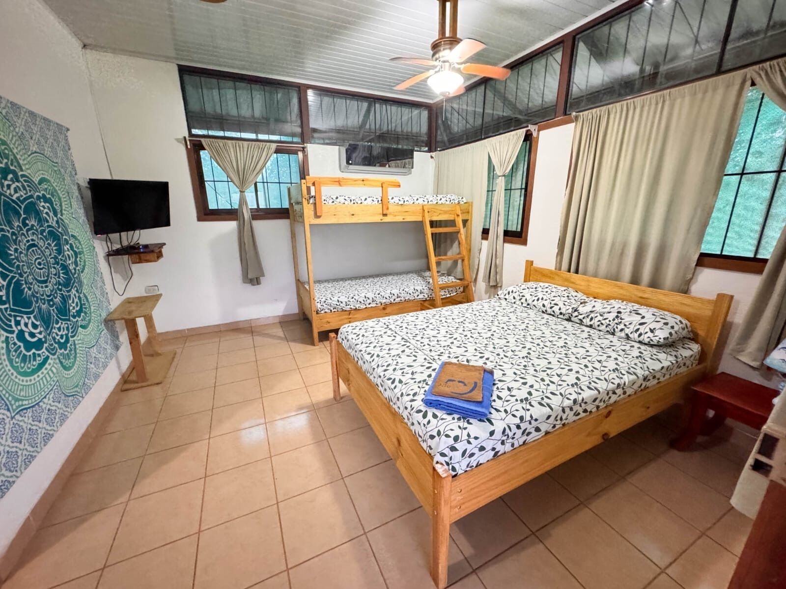 Una habitación con literas, ventilador de techo, televisión y un tapiz estampado.