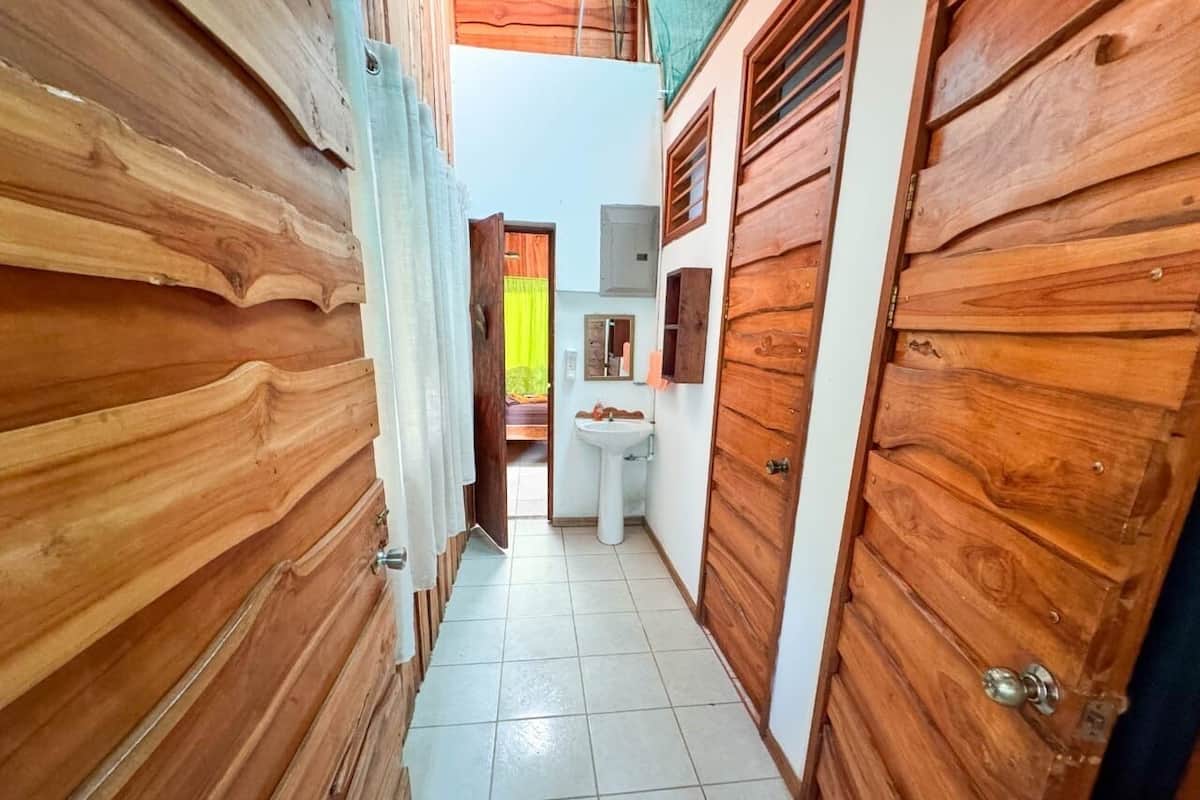 Un pasillo estrecho con paredes y puertas de madera, suelo de baldosas y una pequeña zona con lavamanos.