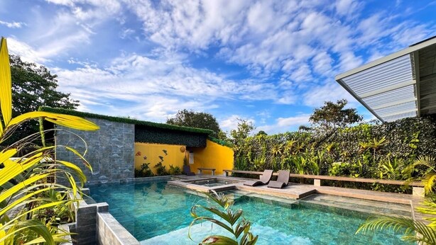 A swimming pool with a stone wall and a yellow building in the background. - Delfines del Golfo (Puerto Jimenez)
