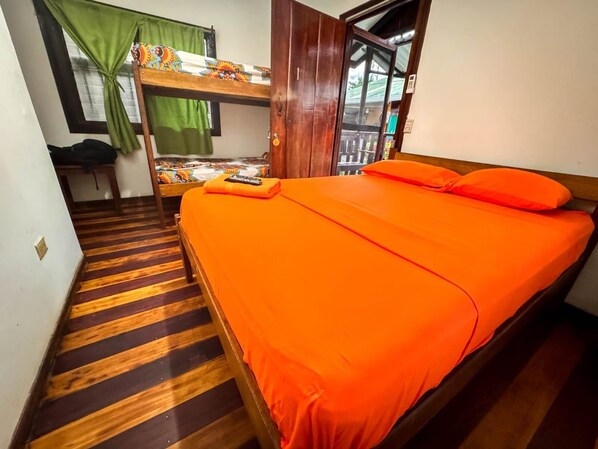 Una habitación con una cama individual superpuesta, una cama individual con ropa de cama naranja, suelo de madera y una ventana con cortinas.